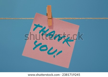 Word THANK YOU written on memo sticky note and isolated on blue background illustrating concept of gratitude.