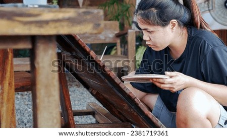 Asian woman painter creating art use a paintbrush to draw lettering designs on a wooden coffee shop sign.outdoor activities,People doing activities.