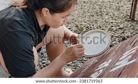 Asian woman painter creating art use a paintbrush to draw lettering designs on a wooden coffee shop sign.outdoor activities,People doing activities.