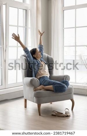 Happy mature woman raised her arms do stretching exercises feel renewed after comfort rest seated on cozy modern armchair in fashionable light living room. Wellbeing, carefree retired relaxing at home Royalty-Free Stock Photo #2381719467