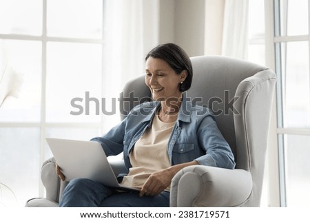 Cheery mature woman laugh while watch on-line comedy movie on digital streaming services, enjoy virtual meeting event with family use video conference application, spend free time with laptop at home Royalty-Free Stock Photo #2381719571