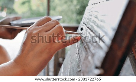 Close-up of Hands of Young woman painter creating art use a paintbrush to draw white lettering designs on a wooden coffee shop sign.outdoor activities,People doing activities.