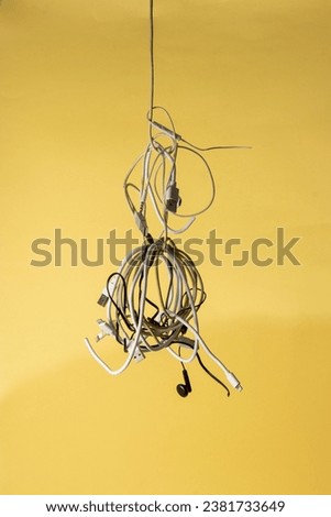 A vibrant yellow wall is the backdrop for a collection of electrical cords and cables dangling from an overhead wire