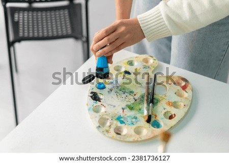 artist's hand squeezing colorful paint out of tube on the palette