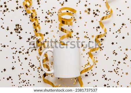 White mockup mug with golden ribbons and glittering confetti stars on white wooden background, top view. Mug with copy space for design and logo. Christmas, New Year and holidays concept