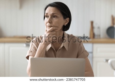 Brooding woman sit at table with laptop in kitchen deep in thought, looks aside, ponder on problem, experiences lack of understanding, thinks on unpleasant news, distracted from work. Tech, complexity Royalty-Free Stock Photo #2381747705