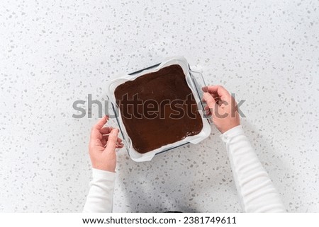 Flat lay. Pouring fudge mixture into the baking pan lined with parchment paper to prepare plain fudge. Royalty-Free Stock Photo #2381749611