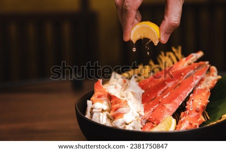 Steamed King crab in Japanese style in black bowl. Hand squeeze lemon with lemon juice drop. Royalty-Free Stock Photo #2381750847