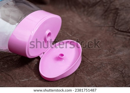 Plastic container with pink opened cap on genuine brown leather background, abstract textures