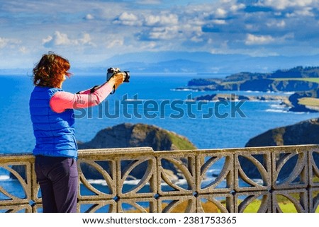 Woman with camera take travel picture from sea landscape, Atlantic ocean and Asturias coast at Cape Penas in north Spain.