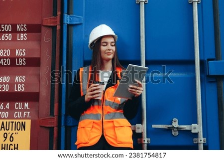 Female Engineer Logist with tablet drinking coffee from paper cup, having a break from work. White helmet and vest in container terminal port or construction site