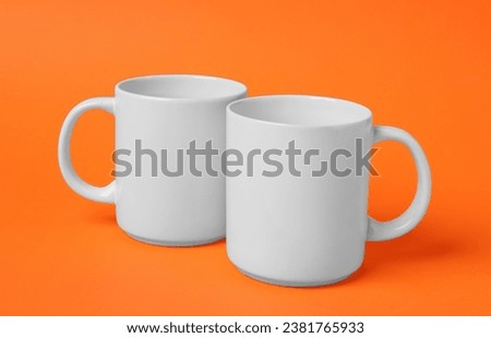 Two white ceramic mugs on orange background Royalty-Free Stock Photo #2381765933