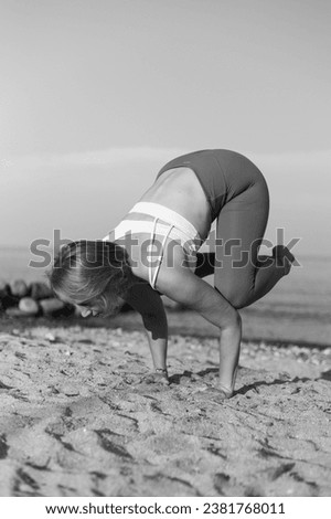 Young pretty woman performing bakasana yoga pose on the beach at sunset