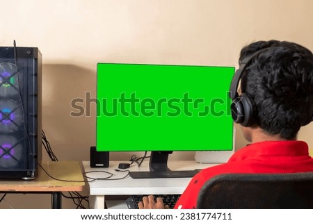 A gamer playing online video game on his powerful personal computer with green screen - shot from back