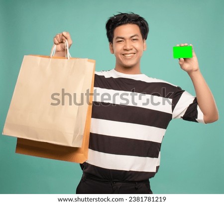 good looking asian man smiling face holding shopping bags and payment cards Wearing a black and white striped shirt.