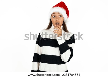 Nervous puzzled Young beautiful woman wearing striped sweater and a santa claus hat at christmas opens mouth from surprise, reacts on sudden news.