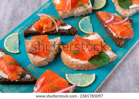 Bruschetta set with smoked trout slices, cream cheese and capers on wheat and rye bread. Appetizers on blue board Royalty-Free Stock Photo #2381785097