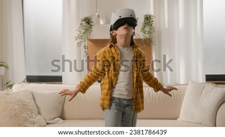 Funny happy kid girl playing online video 3d game using virtual reality headset child schoolgirl play in vr glasses at home in living room explore cyberspace world metaverse innovative technology AR