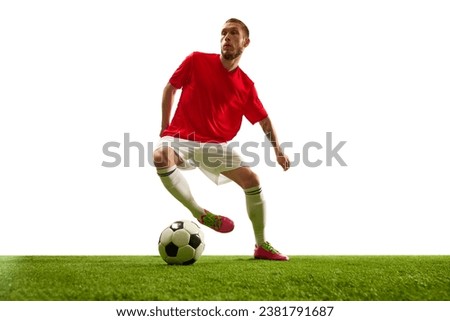 Professional soccer player looks confident in sportwear and boots training kicking ball for goal in jump against white background. Football school. Concept of game, sport, recreation, active lifestyle