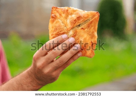 Guy's hand holds a puff pastry with cheese, snack and fast food concept. Selective focus on hands with blurred background and copy space for text.