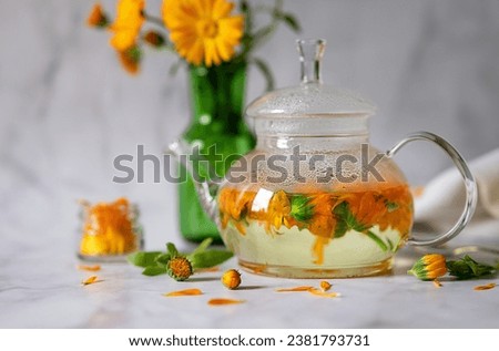 Cup of marigold tea and calendula flowers outdoors on green background.
