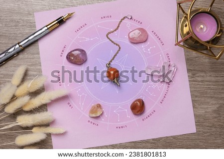 Astrology prediction. Zodiac wheel, gemstones, pendulum and burning candle on wooden table, flat lay