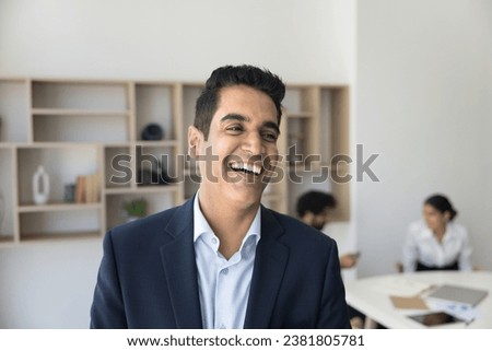 Cheerful Indian business team leader man posing for head shot in office meeting room, laughing, looking away with toothy smile. Handsome middle aged executive professional casual portrait