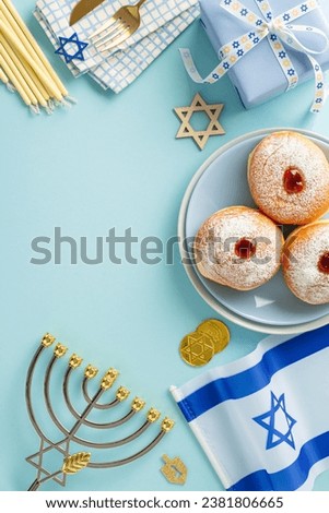 Experience Hanukkah's beauty with top-view vertical image of sufganiyot, utensils, Star of David, Israel's flag, giftbox, menorah candle holder, gelt against pastel blue backdrop for text or advert