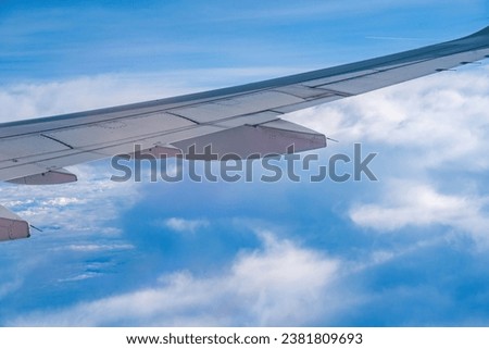 View from airplane window at the sky. Blue sky and fluffy white clouds from airplane window view, jet engine on the wing. Booking airline ticket - airplane window seat. Selective focus