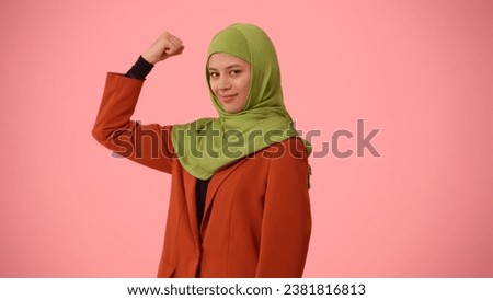 Medium-sized isolated photo capturing an attractive young woman wearing a hijab, veil. She is showing her muscles, expressing confidence.