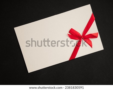 A white sheet of paper with a red satin bow on a black background. Space for text.