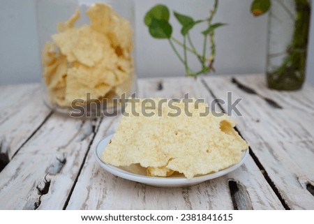 Indonesian Rice Crackers "Gendar" on a white plate on a white wooden table background. Gendar crackers are crackers made from rice dough that are seasoned with spices and flavor enhancers