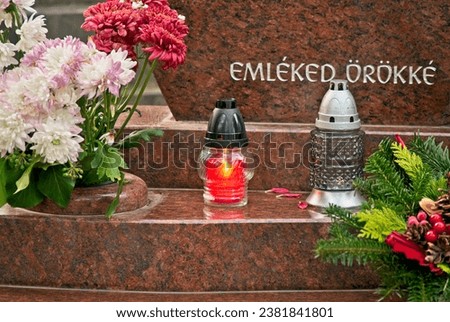 Candle (snitch) on a tombstone in a cemetery during the day in Hungary with a Hungarian sign " Emléked örökké" which means "Your memory forever". All Saints' Day.