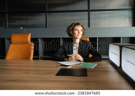 Young businesswoman waiting for start of meeting. Corporate woman in suit sitting in office, working on documents, waiting for client.