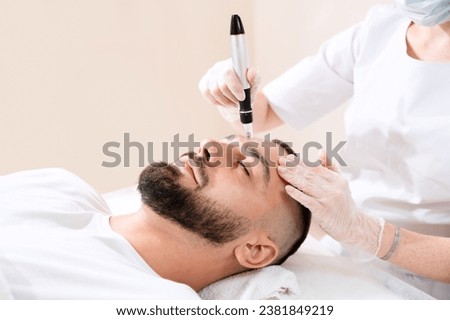 Dermastamp fractional mesotherapy treatment for man in cosmetology clinic. Royalty-Free Stock Photo #2381849219