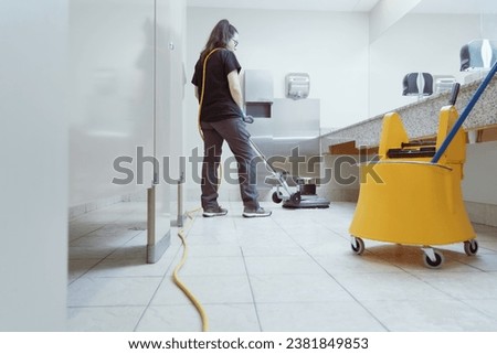 woman scrubbing the bathroom floor with an industrial scrubbing machine Royalty-Free Stock Photo #2381849853