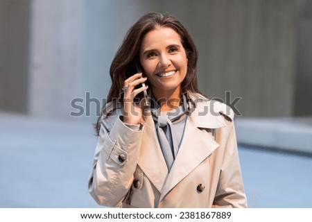 Cheerful european middle aged businesswoman talking on smartphone, walking outdoors near modern office center. Brunette pretty lady entrepreneur having phone talk Royalty-Free Stock Photo #2381867889