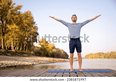 Mid aged man practicing yoga outdoor. Caucasian man using yoga mat and standing with raising arms on nature. Sun salutation. Royalty-Free Stock Photo #2381871997