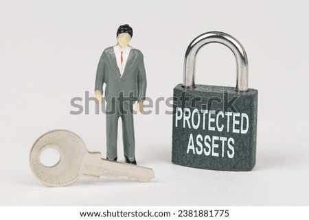 Business concept. On a white surface there is a figurine of a businessman, a key and a lock with the inscription - Protected Assets Royalty-Free Stock Photo #2381881775