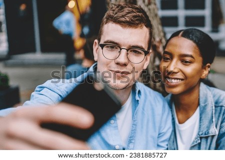 Cheerful diverse friends taking pictures on mobile phone resting outdoors