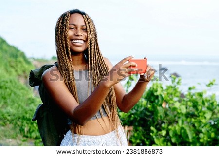 positive female tourist with dark skin taking photos on cellular travelling on island