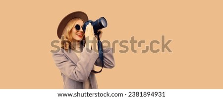 Portrait of stylish happy smiling woman photographer with digital camera taking picture wearing round hat, coat on studio background, blank copy space for advertising text