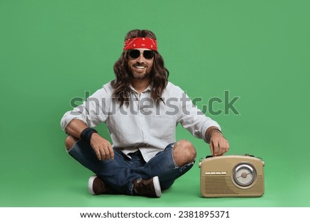 Stylish hippie man in sunglasses turning on radio receiver against green background Royalty-Free Stock Photo #2381895371