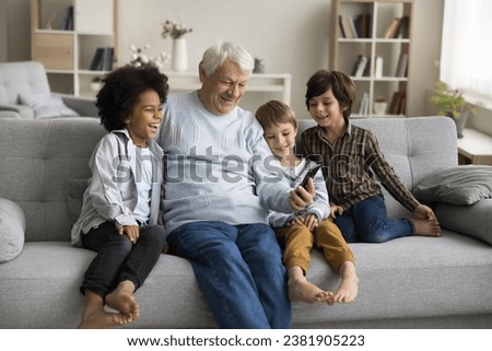 Happy multigenerational family enjoy videocall using smartphone, great-grandad and great-grandsons having fun use new mobile application, look at phone screen laugh, watch video spend time on internet