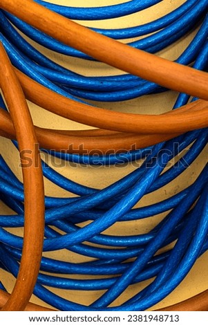 Orange and blue garden hose. Pile of a tangled long hose or cable wire background texture. Water rubber tube. Plastic pipe. Royalty-Free Stock Photo #2381948713