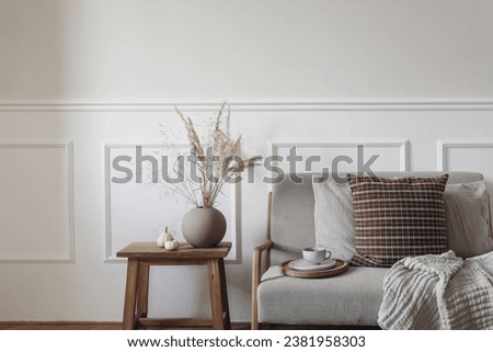 Dry grass bouquet in ball shaped vase. Midcentury sofa with cup of coffee, checkered linen cushions, blanket. Little white pumpkins, old side table. Autumn interior. Thanksgiving, Halloween.