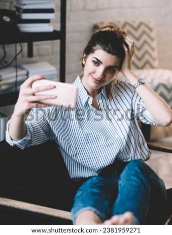 Cute young woman taking picture of smartphone in modern apartment