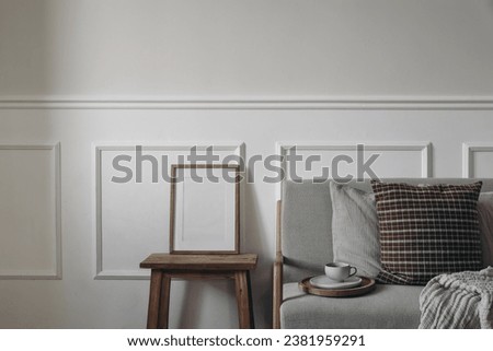Blank wooden picture frame mockup on vintage side table, night stand. Linen midcentury sofa. Cup of coffee, checkered brown and beige cushions. Moody interior. Elegant home, living room. Blank wall.
