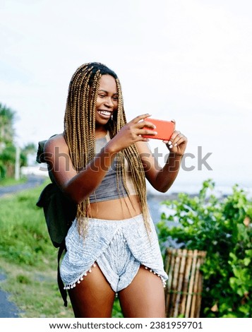 positive dark skinned tourist with dreads taking pictures on mobile phone during summer trip