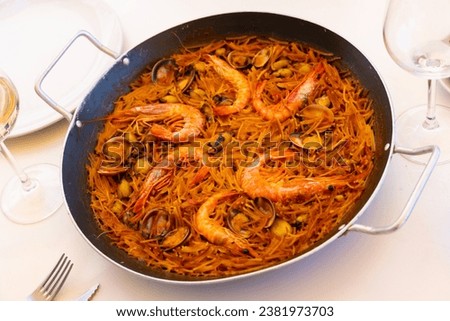 Appetizing racy seafood fideua with mussels, scallops and prawns served with aioli sauce in traditional paella pan. Authentic Valencian cuisine Royalty-Free Stock Photo #2381973703